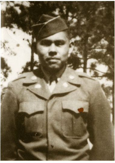 Black and white vintage photo of war hero Charles George, in uniform with a military cap and insignia visible, standing in front of a background of trees.
