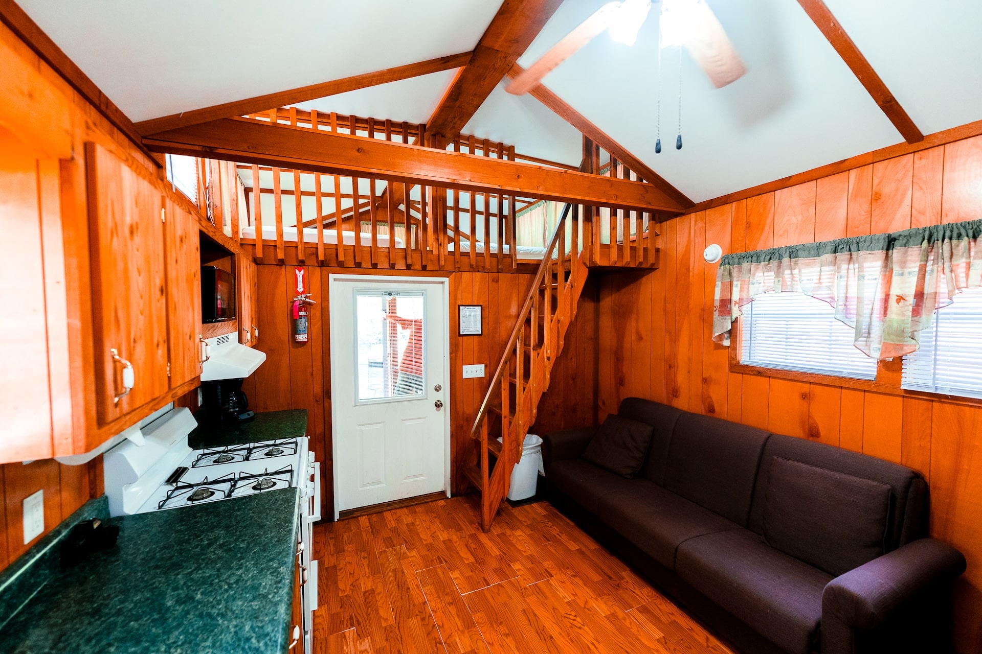 Cozy space inside a cabin featuring a couch, windows, staircase, and stove.