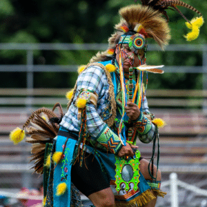 performers wearing vibrant traditional attire perform a dance at a 4th of July powwow, while spectators watch.