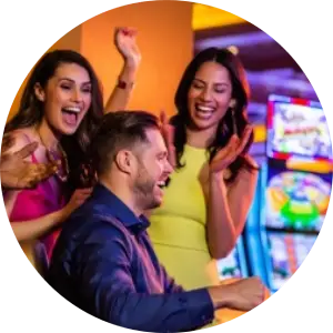 Two women and a man, joyfully engaging at a brightly lit Harrah's casino, with colorful slot machines in the background.