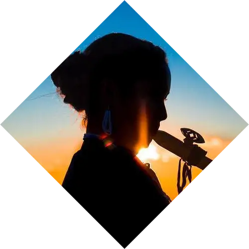 Silhouette of a woman holding a feather to her lips during sunset, framed within an updated diamond-shaped border against a vibrant orange sky.