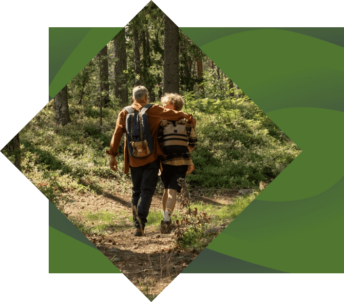 Two elderly people with backpacks walking arm-in-arm along a forest trail, viewed from behind, enclosed in a diamond-shaped frame with a green border.