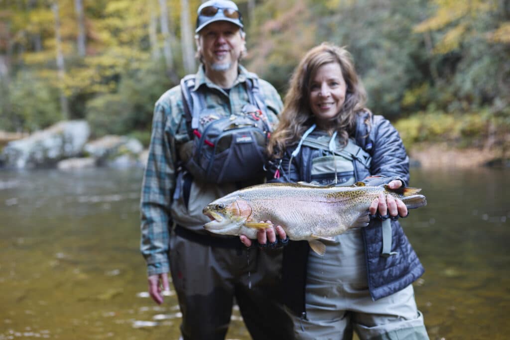 two people in fishing gear fly fish in Cherokee smile while showing large fish caught in Cherokee