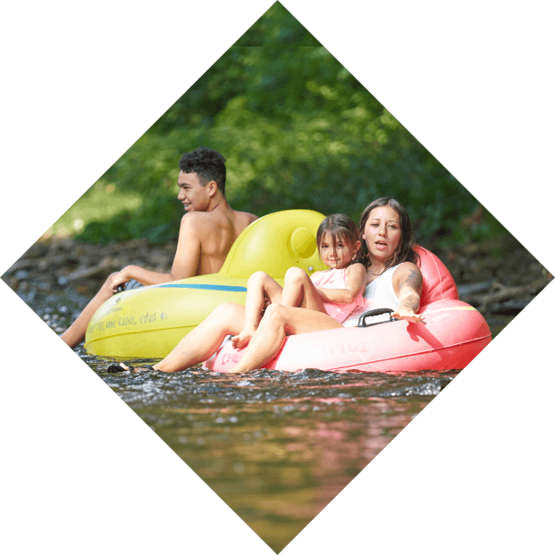 people leisurely float on colorful inflatables in a serene river surrounded by lush greenery while tubing under sunlight.