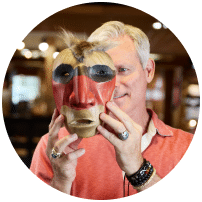 man holding up painted wooden mask