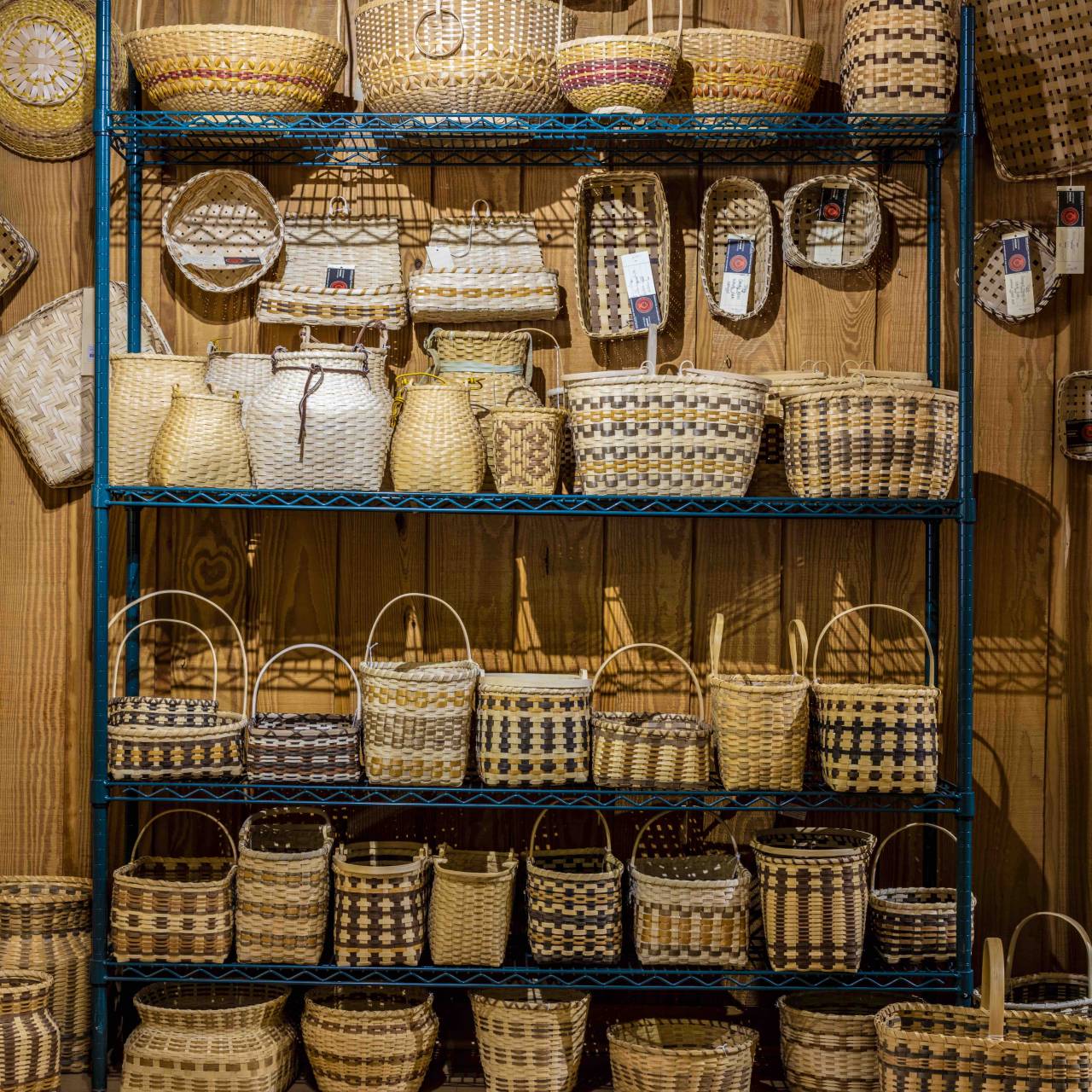 A variety of handcrafted Cherokee baskets displayed on wooden shelves, featuring different sizes, patterns, and weaving techniques. Each basket is uniquely designed with natural tones.