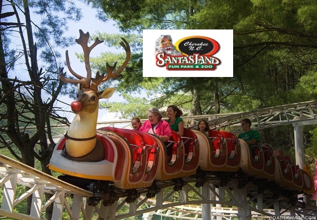 A roller coaster ride shaped like a reindeer leads a train of excited passengers through a wooded area. The ride features a prominent Rudolph nose and antlers, with a logo for "Santa's Land