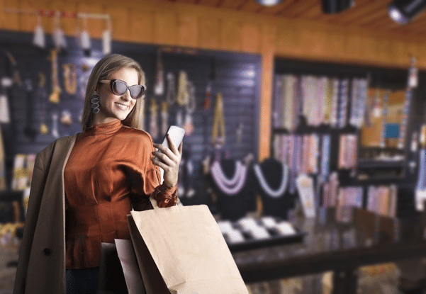 smiling female in trendy wear and stylish sunglasses standing with paper shopping bags
