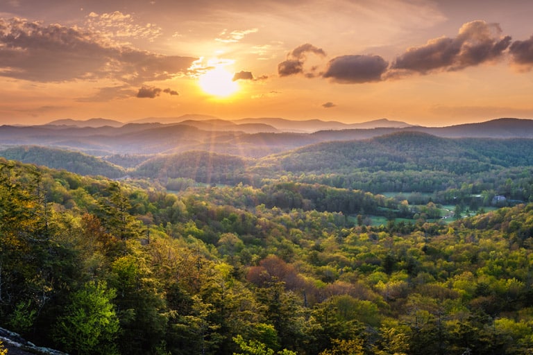 Sunset over a lush, rolling landscape with layers of forested hills under a vibrant sky, highlighting the natural beauty and tranquility of a rural area perfect for play or recreational activities.
